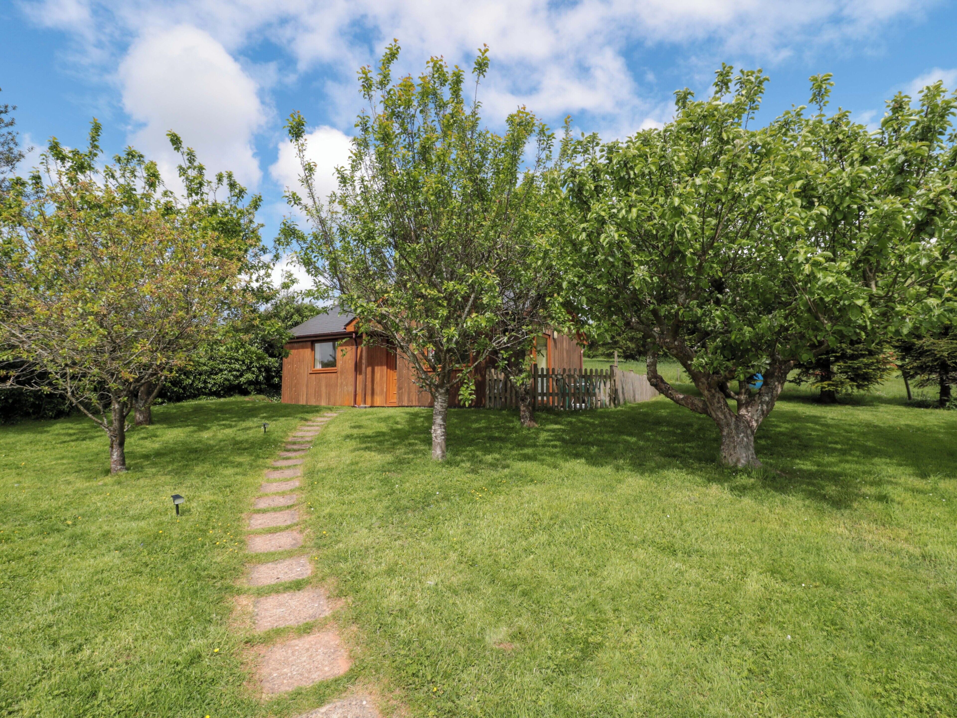 A wooden cabin with a stone pathway leading to it, surrounded by lush green grass and trees.