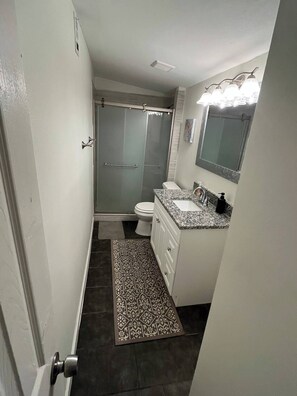 Un baño con ducha, inodoro, lavabo y una alfombra estampada.