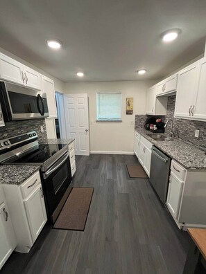 A modern kitchen with white cabinetry, stainless steel appliances, and a gray floor. - Econo Comfort near TCU & Downtown (Fort Worth)
