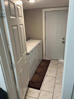 A laundry room with a washing machine and dryer, a patterned rug, and a white door. - The Yellow Cottage near TCU & Downtown Ft. Worth (Fort Worth)