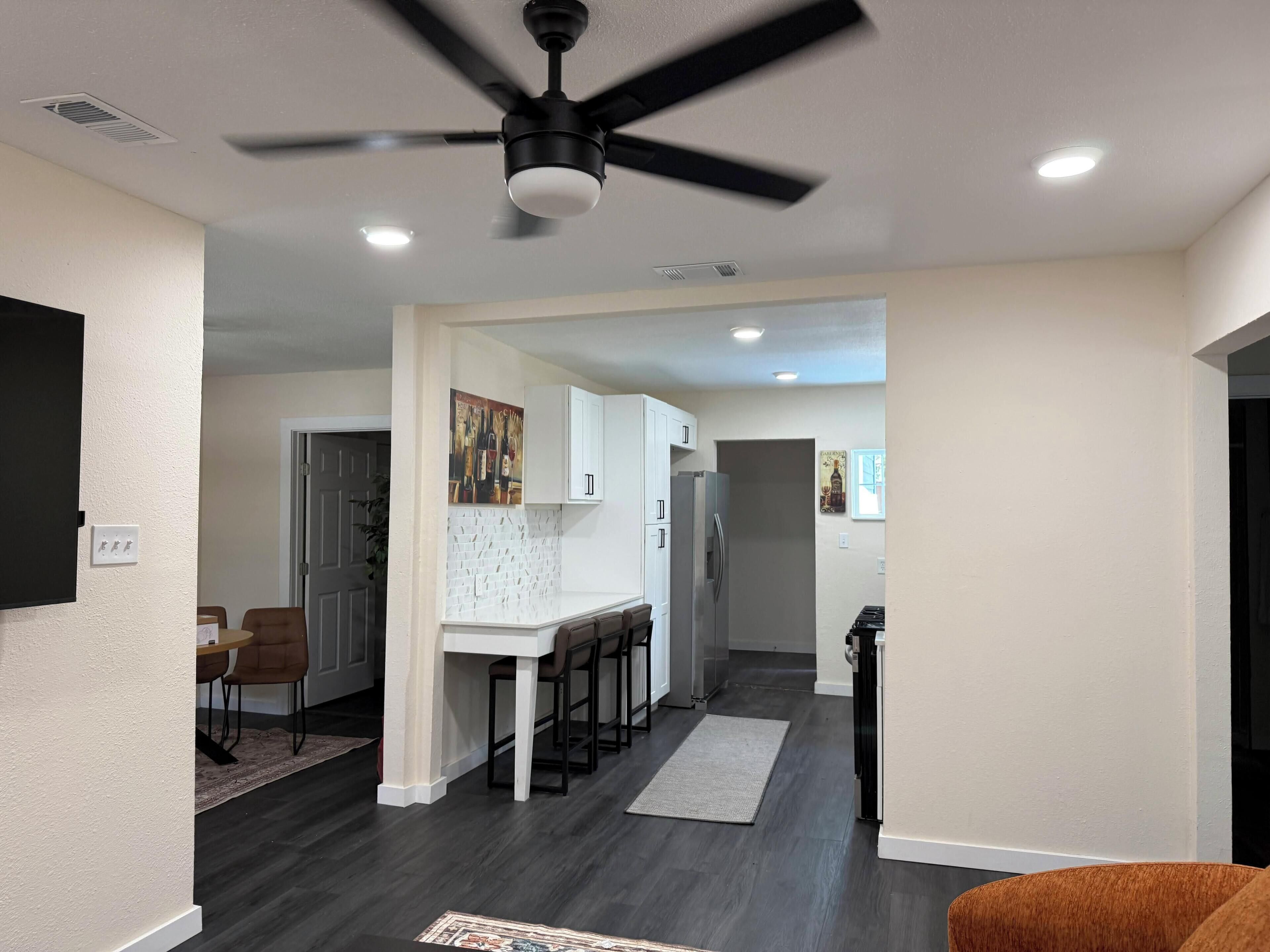 A modern kitchen with white cabinets, a stainless steel refrigerator, and a ceiling fan.