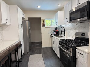 A modern kitchen with white cabinets, a stainless steel refrigerator, a black stove, and a microwave. - Comfortable & Modern Home near TCU-Downtown-Shops (Fort Worth)