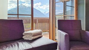 Une chambre avec un balcon, deux fauteuils violets et une pile de serviettes pliées.