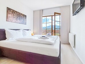Ein Hotelzimmer mit Bett, einem Bild an der Wand, einem Fenster mit Bergblick und einem an der Wand befestigten Fernseher.