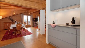 Ett modernt kök med grå skåp, en matplats med en röd matta, trägolv och ett träpanelat tak.