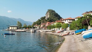 A lakeside village with boats docked along the shore, a pier, and buildings with red-tiled roofs.