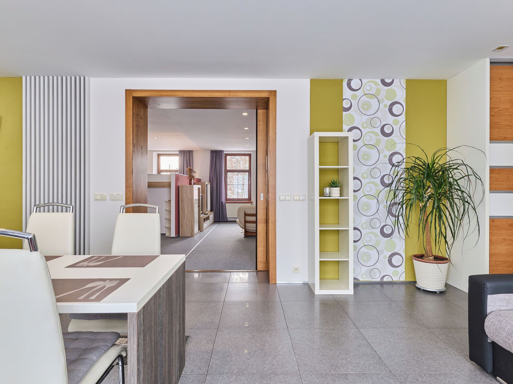Una habitación de hotel moderna con comedor, cocina al fondo y una planta en maceta.