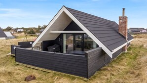 Una cabaña moderna con techo negro, puerta de cristal, un pequeño patio y una chimenea.