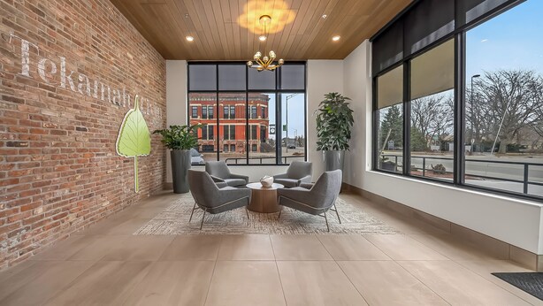 A modern interior with a brick wall, large windows, and a seating area with a round table. - Bright New 2BR in Tekamah at Tiger Town (Tekamah)