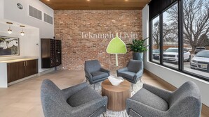 A modern interior with grey armchairs around a wooden coffee table, a brick wall, and a large window with a view of parked cars. - Bright New 2BR in Tekamah at Tiger Town (Tekamah)