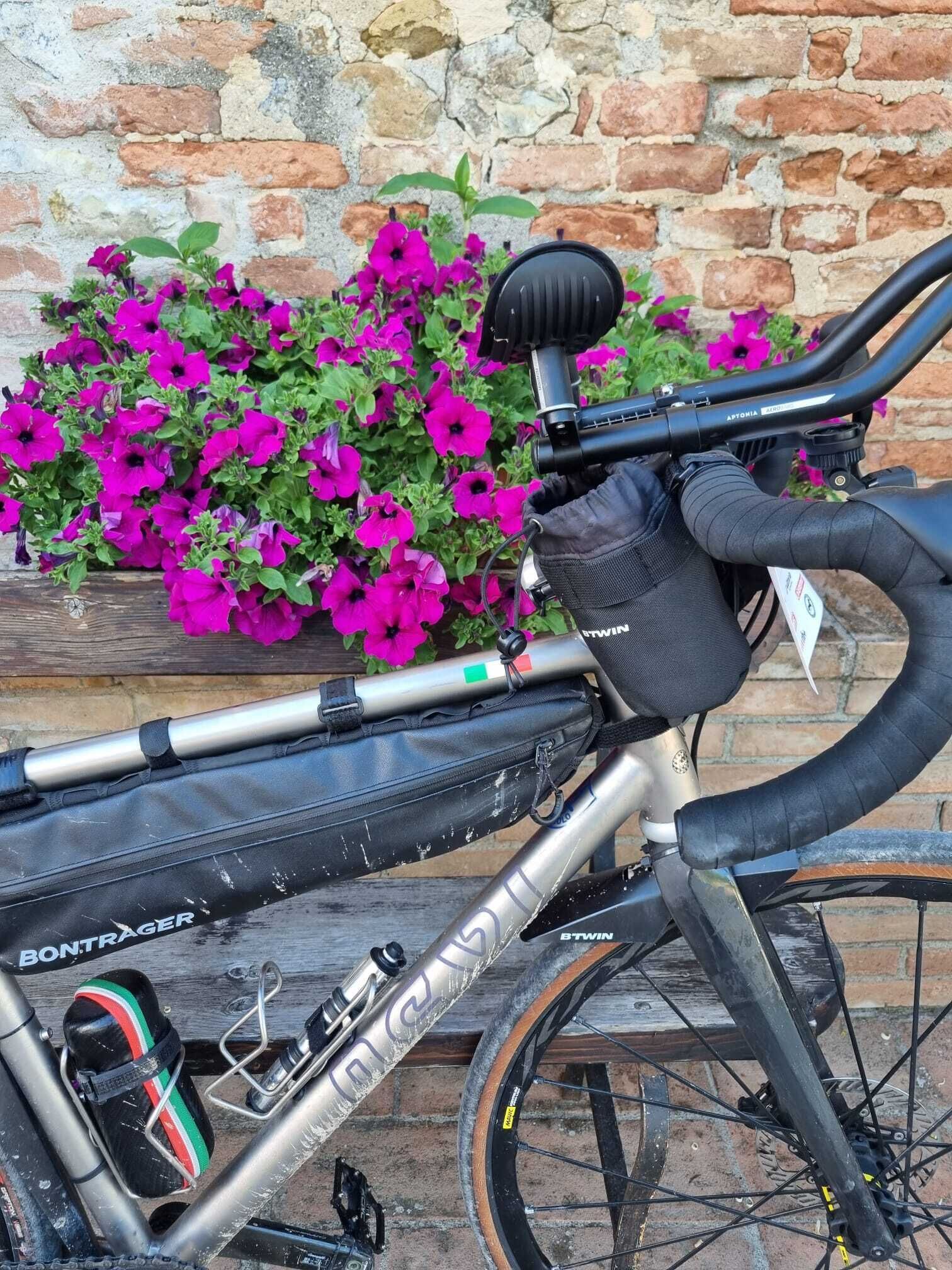 Een fiets met een zwarte tas bevestigd aan het frame, een drinkfles en een paar schoenen.