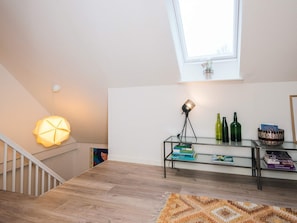 Un espacio habitable moderno con una escalera, una mesa de vidrio con libros y adornos, una lámpara de pie y un ventanal con vistas.