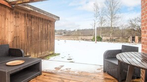 En udendørs terrasse med fletningsmøbler, et trædæk og udsigt over et sneklædt landskab.