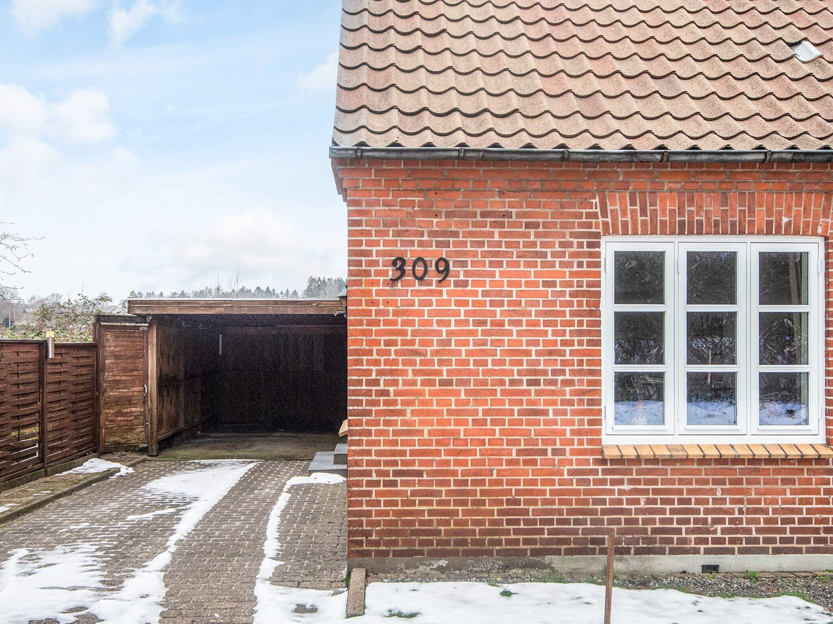 A brick house with the number 309 on the wall, a window, and a covered driveway.