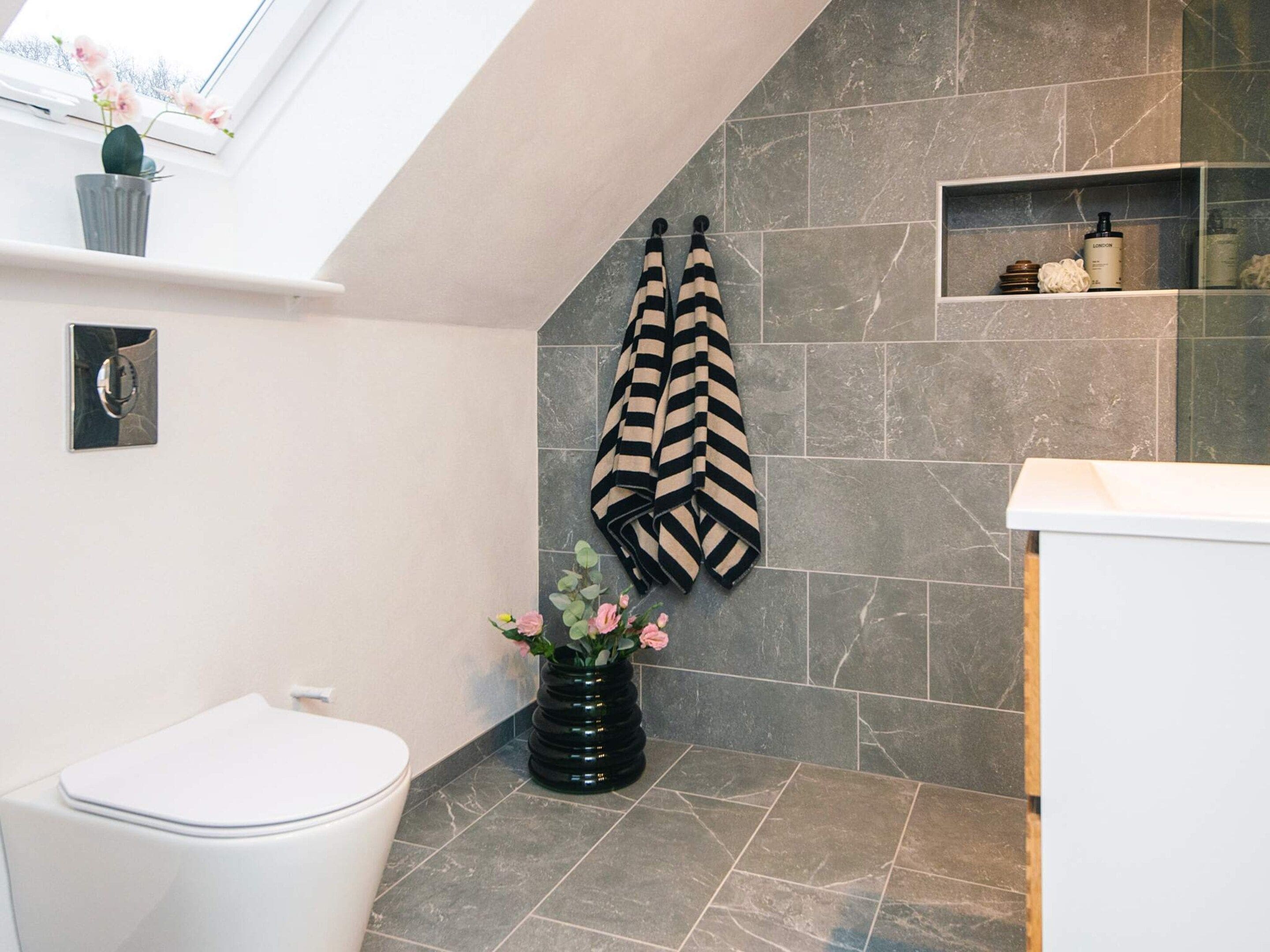 A bathroom with a white toilet, a black vase with pink flowers, and a striped towel hanging on the wall.