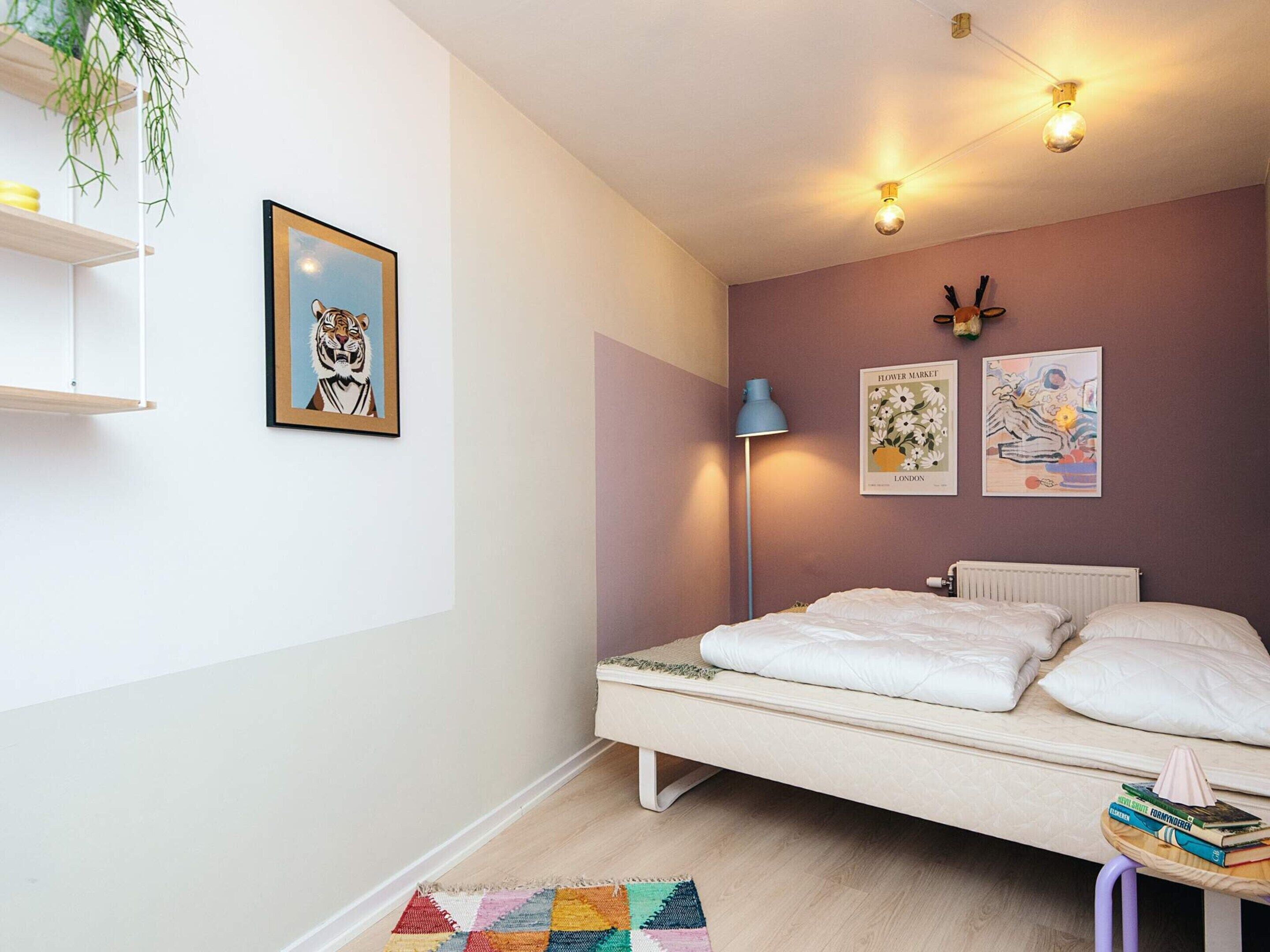 Een slaapkamer met een bed, een nachtkastje met boeken, een vloerlamp en wanddecoratie.
