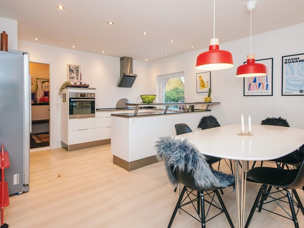 A modern kitchen with a central island, a dining area with a round table and chairs, and a living space with a sofa and a TV. - 4 Star Holiday Home in Kjellerup (Kjellerup)