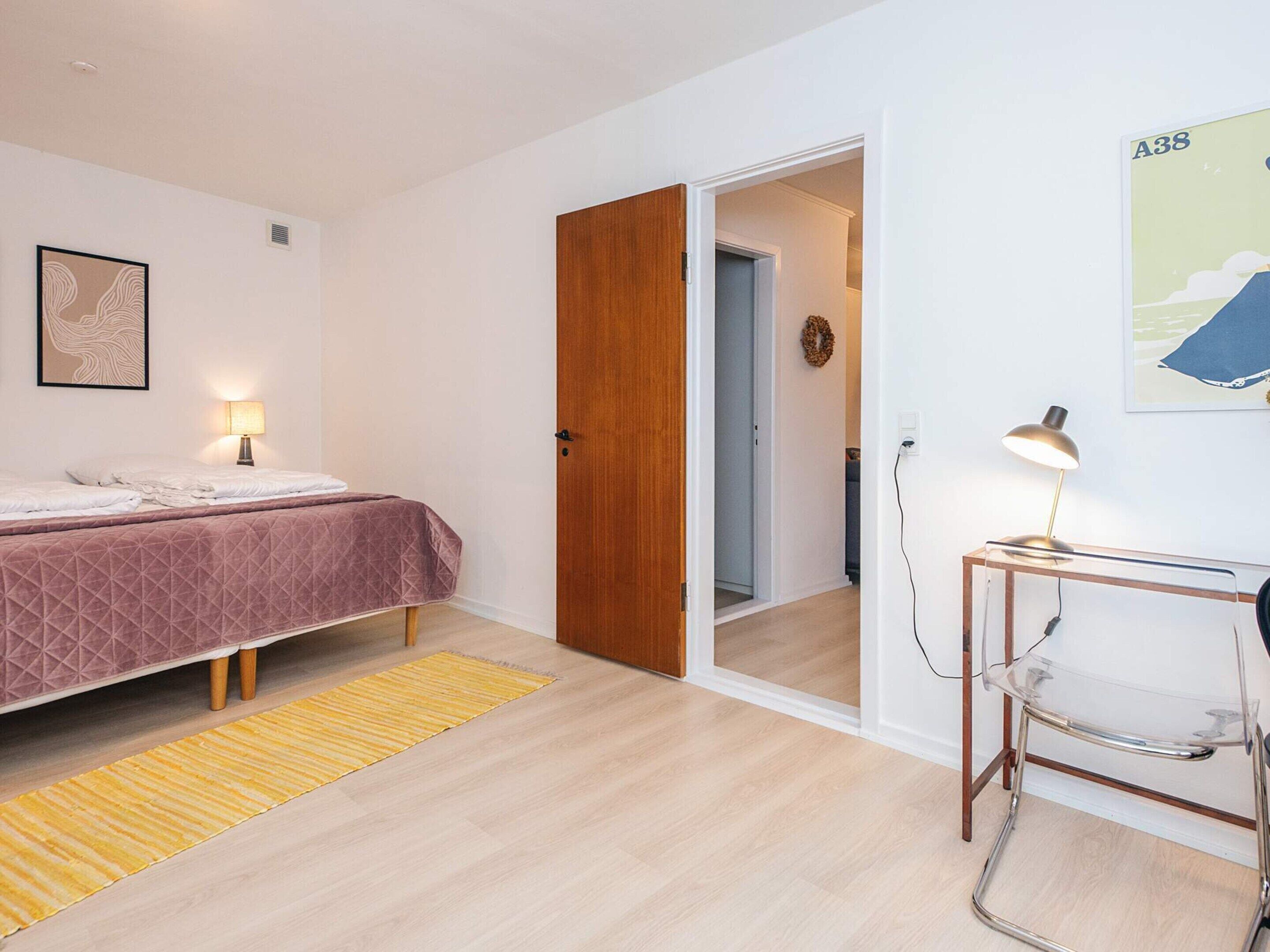 Une chambre à coucher avec un lit, un bureau, une chaise, une porte et un mur orné d’un tableau.