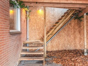 Una scala in legno conduce a un'area esterna con pavimento di legno, un muro in mattoni e una finestra.