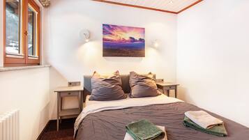 A bedroom with a bed, two bedside tables, a nightstand, a window, and a painting on the wall.