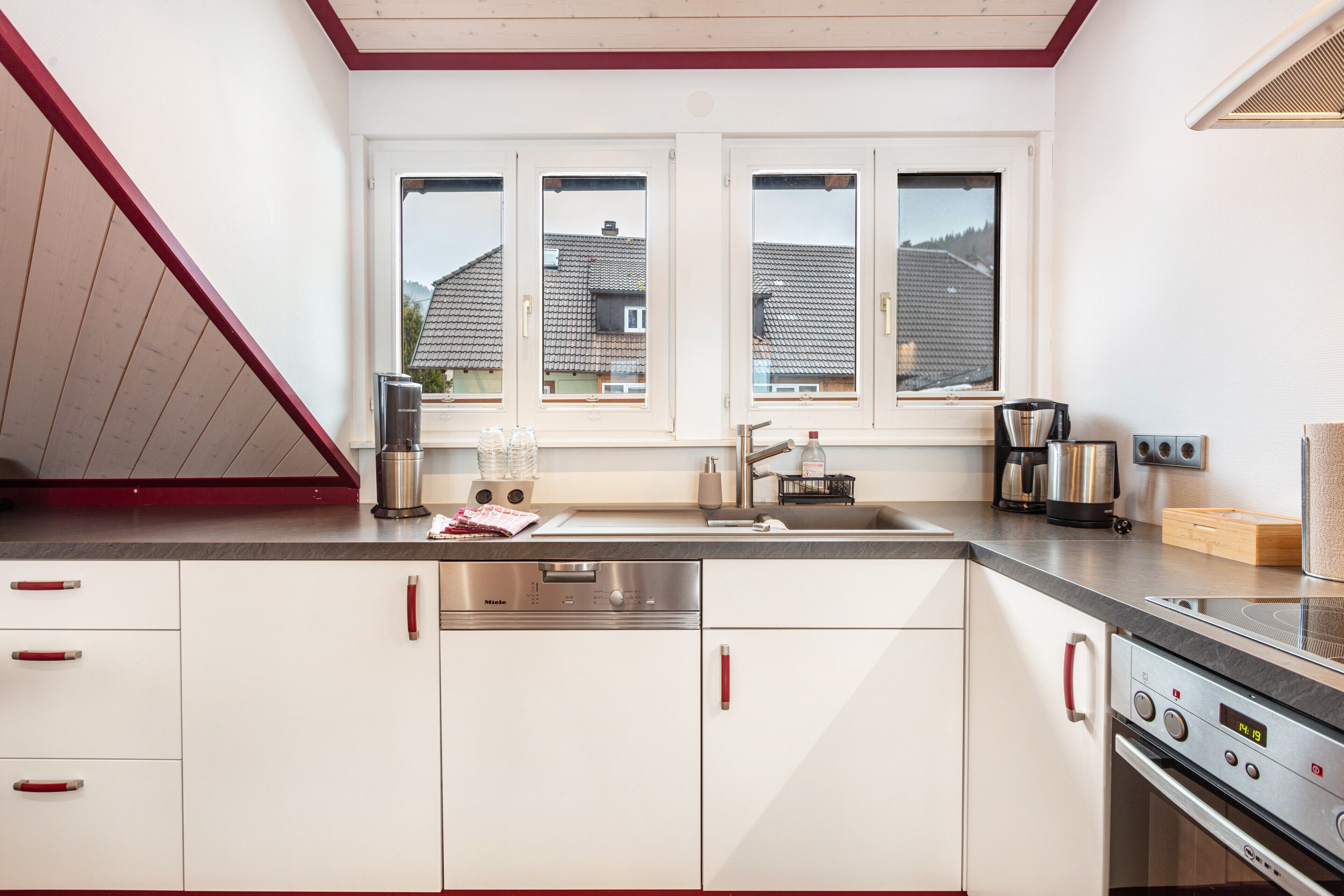 A modern kitchen with white cabinets, stainless steel appliances, and a window with a view of houses.