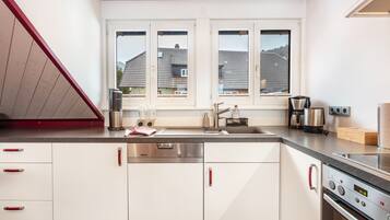 A modern kitchen with white cabinets, stainless steel appliances, and a window with a view of houses.