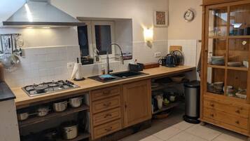 Una cocina con estufa a gas, armarios de madera, un lavamanos y un reloj en la pared.