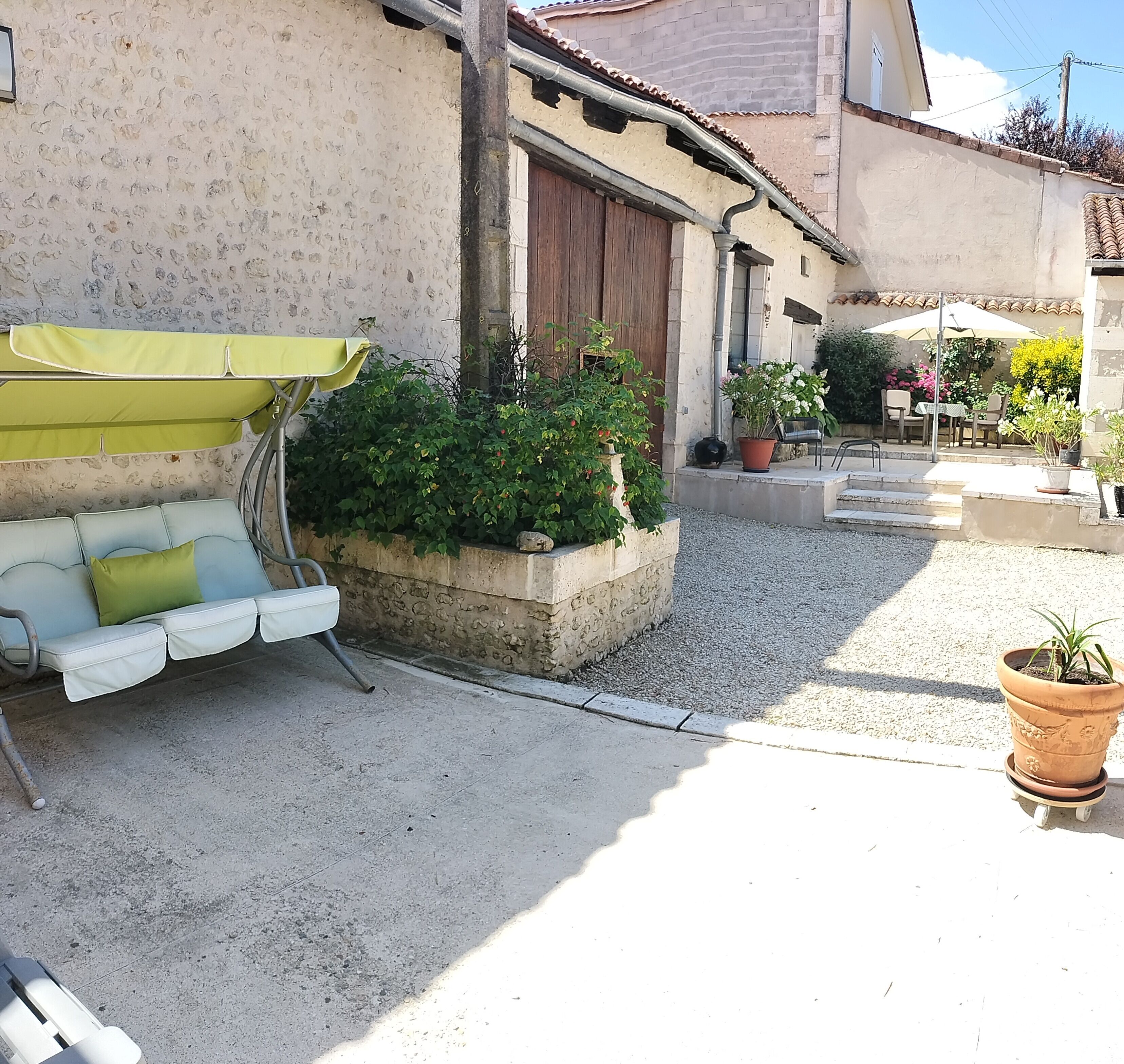 Une cour avec un canapé d’extérieur blanc, un parasol vert et des plantes en pot.