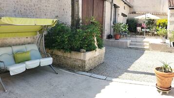 Une cour avec un canapé d’extérieur blanc, un parasol vert et des plantes en pot.