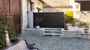 Un patio de grava con un banco de madera, una pantalla negra y plantas en macetas.