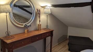 A cozy attic bedroom with a wooden dresser, a round mirror, two lamps, and a black sofa.