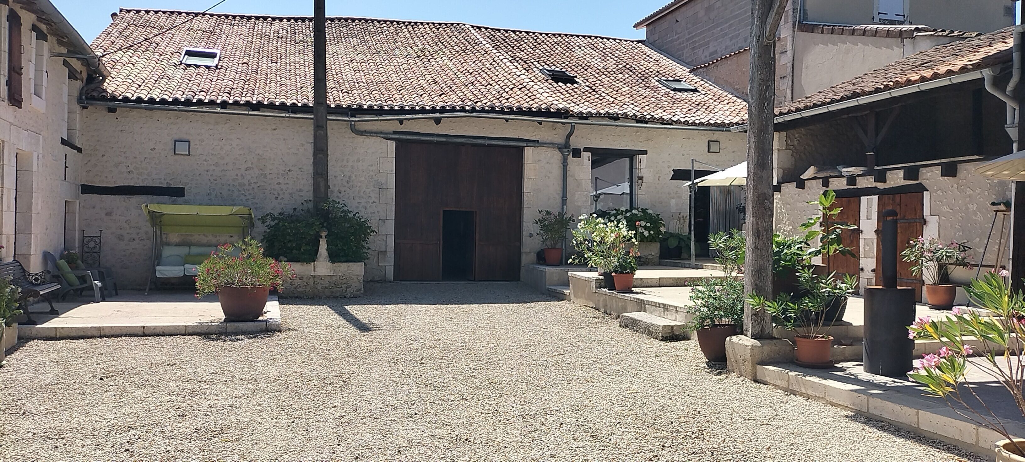 Une cour avec un sol de gravier, un bâtiment doté d’un toit en tuiles et des plantes en pot.