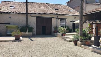 Une cour avec un sol de gravier, un bâtiment doté d’un toit en tuiles et des plantes en pot.