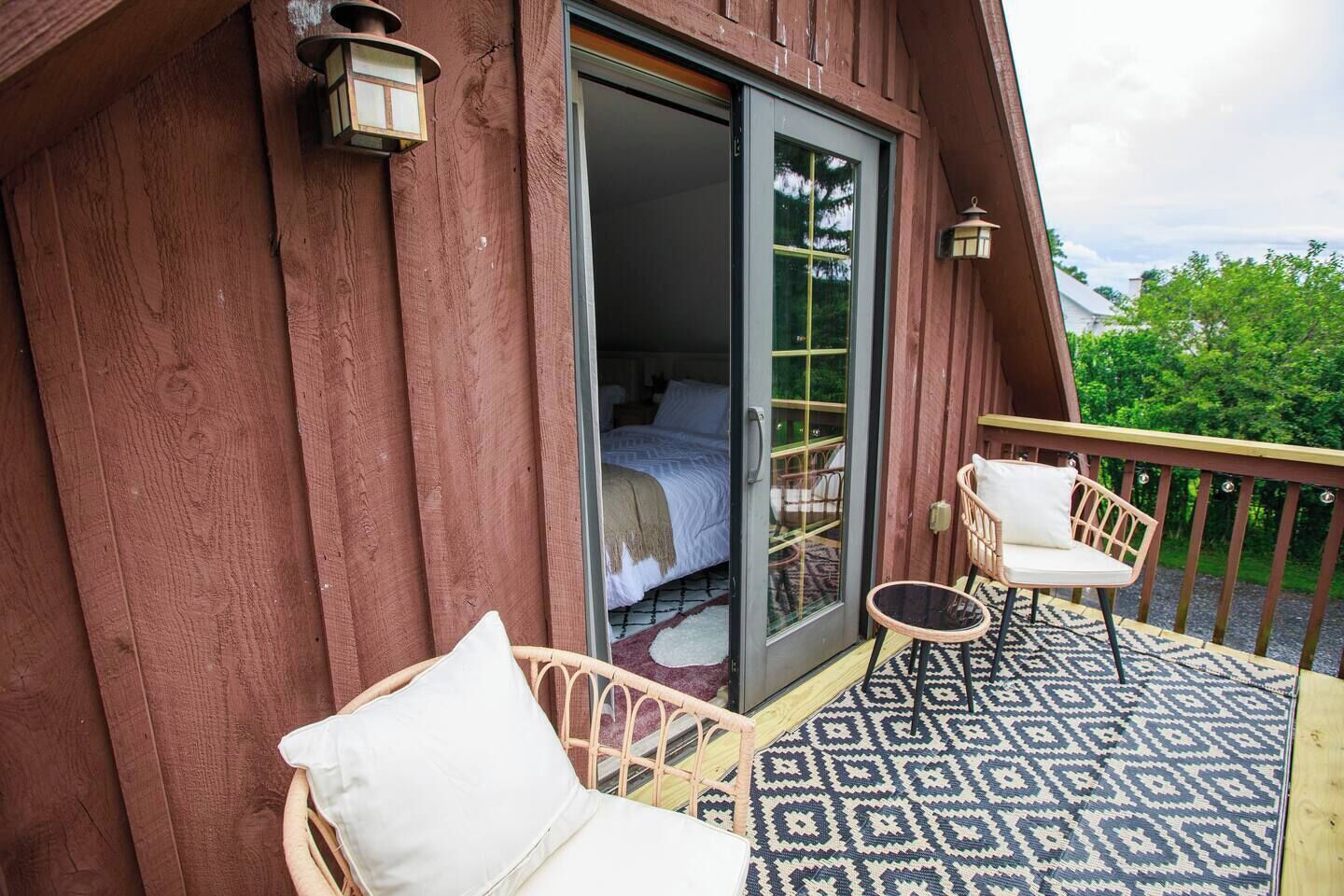 Une cabane en bois dotée d’un balcon où se trouvent deux fauteuils en osier et un tapis à motifs.