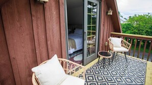 Una cabaña de madera con un balcón que tiene dos sillas de mimbre y un tapete estampado.