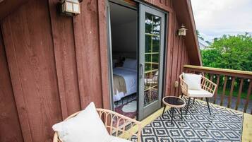 Une cabane en bois dotée d’un balcon où se trouvent deux fauteuils en osier et un tapis à motifs.