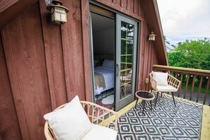 Eine Holzhütte mit einem Balkon, ausgestattet mit zwei Korbstühlen und einem gemusterten Teppich.