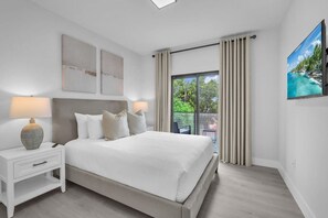 Ein modernes Schlafzimmer mit einem großen Bett, einem Nachttisch, einer Lampe und Blick ins Grüne durch das Fenster.