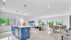 A modern kitchen with a blue island, a dining area with a wooden table and chairs, and a living room with a sofa and a coffee table. - Miami Palm Villas - Family - Entire 8BR-6BA (Miami)
