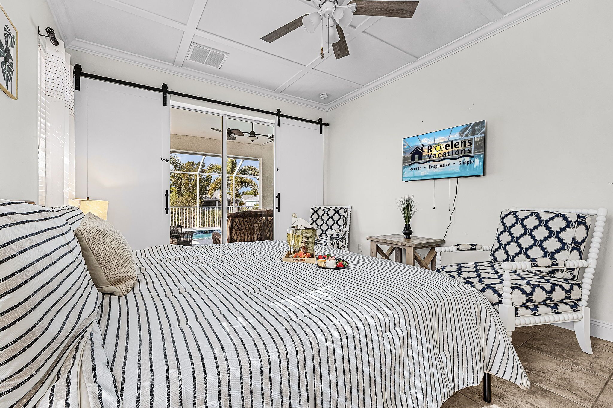 Ein Schlafzimmer mit einem Bett, einem Sessel, einem Tisch und einem Fernseher an der Wand.
