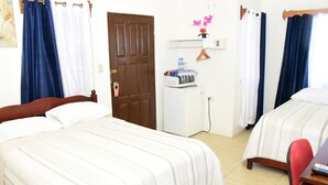 Habitación de hotel con dos camas, un escritorio pequeño con una silla, un refrigerador y una puerta con cortina.