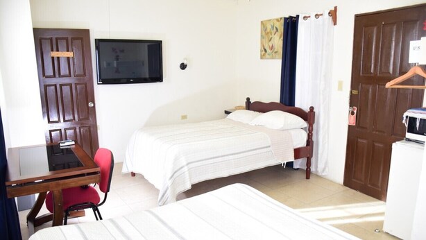 Un dormitorio con dos camas individuales, un escritorio con silla, un televisor en la pared y una puerta con perchero.