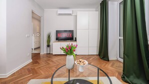 Un salon avec un téléviseur à écran plat, un vase rempli de fleurs et une petite table sur laquelle sont posés des biscuits.