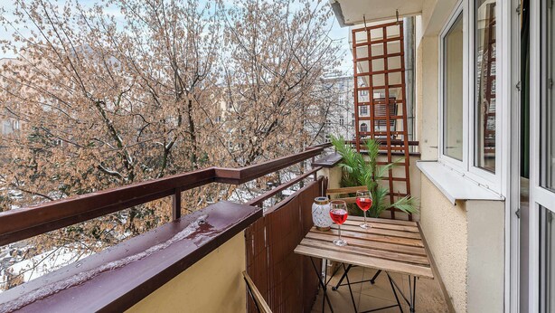 Un balcon avec une table en bois, deux verres à vin et une plante en pot.