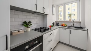 Une cuisine moderne avec des armoires blanches, une cuisinière encastrée et une fenêtre donnant sur un immeuble.