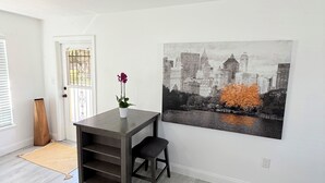 A room with a dark wooden table and a chair, a large cityscape painting on the wall, and a door with a metal gate. - Serenity Oaks A Peaceful Hideaway In LWR (Bradenton)