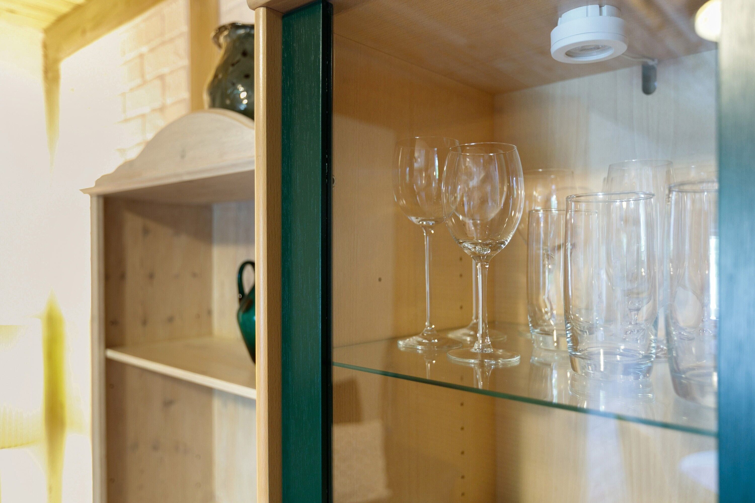 Ett vitrinskåp i glas med vinglas och en hylla med grön ram.