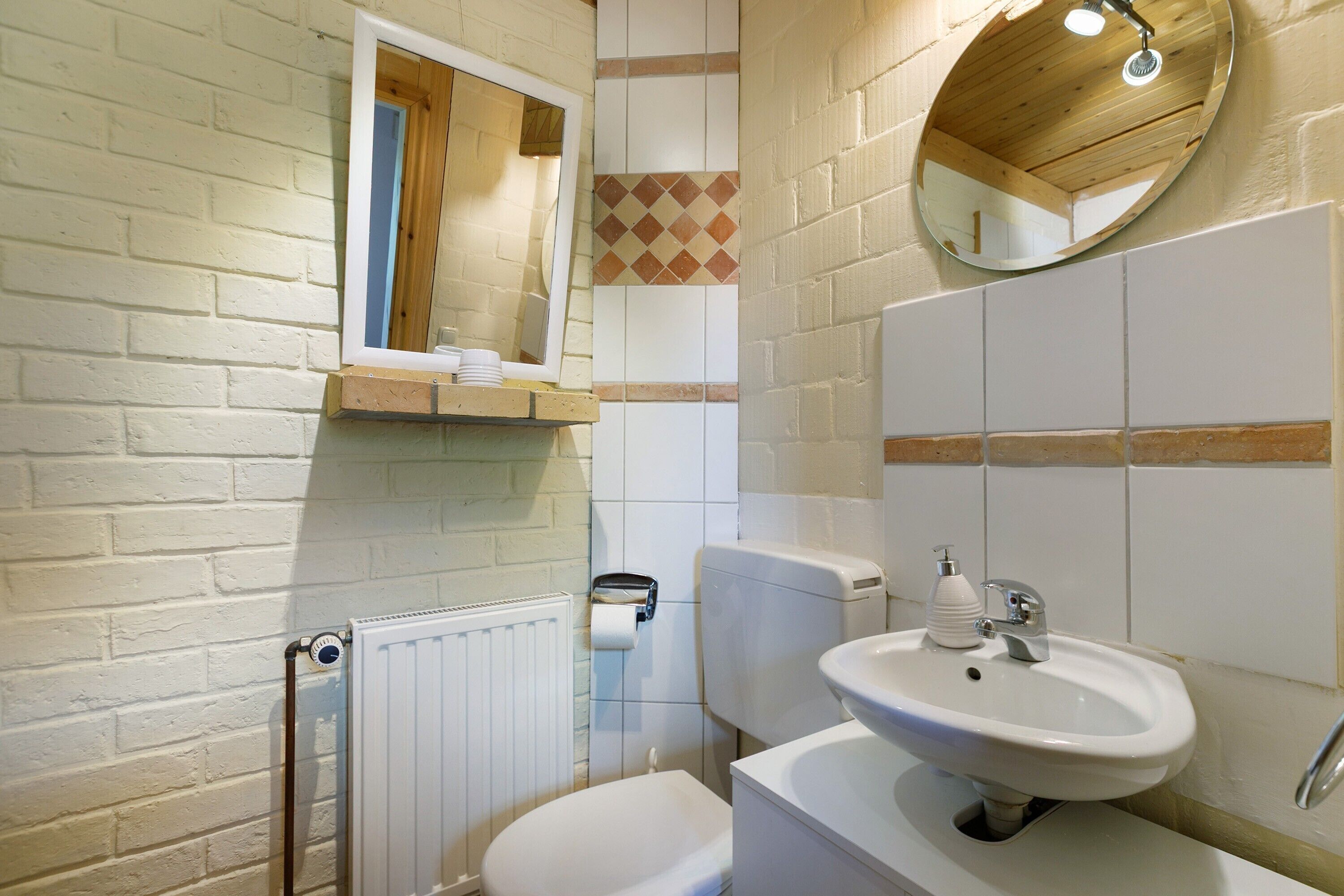 A bathroom with a white toilet, a white sink, a mirror, and a towel dispenser.