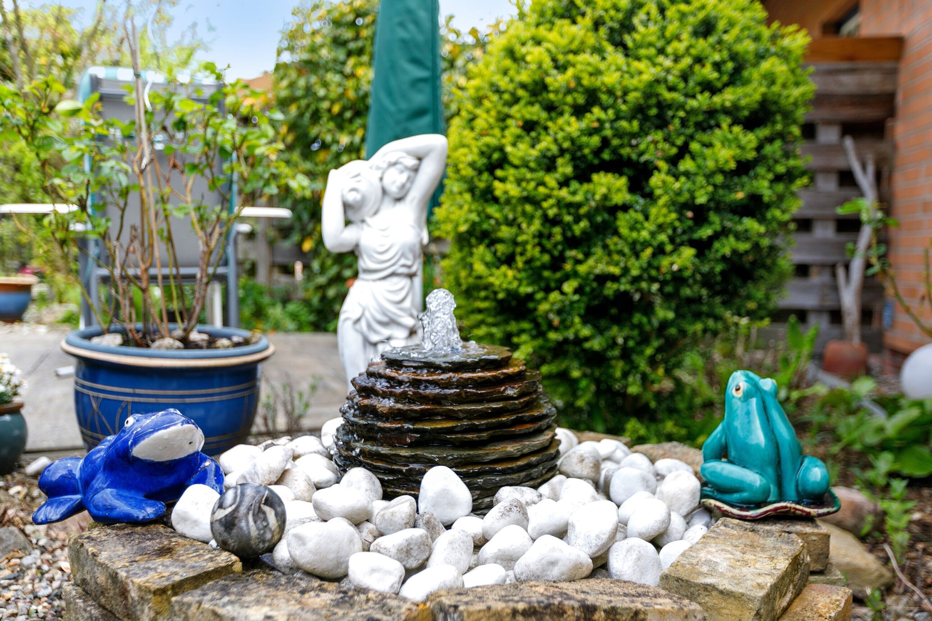 A garden with a fountain, a statue, and a frog sculpture.