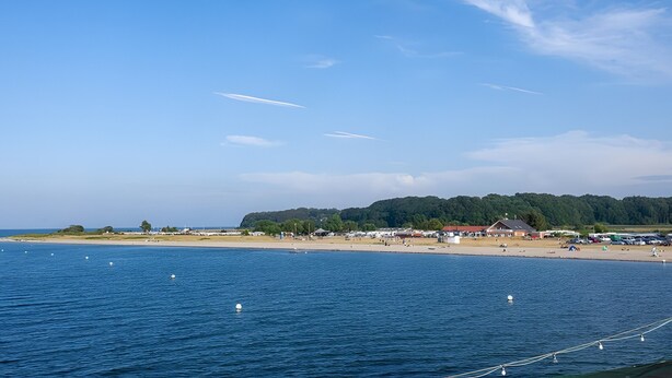 A coastal area with a beach, a forested hill, and a clear sky.